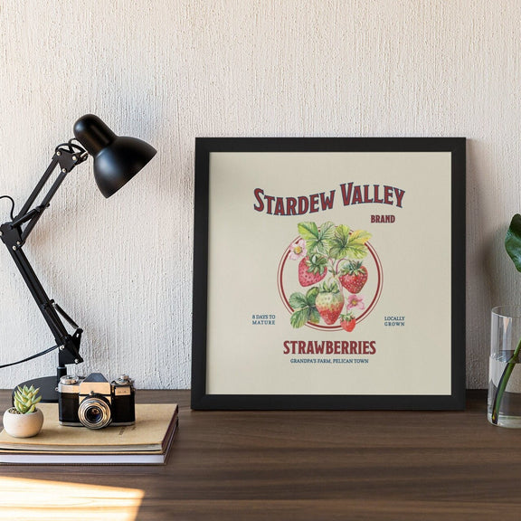 A small Stardew Valley Strawberries Print by New Save in a black frame on a desk.