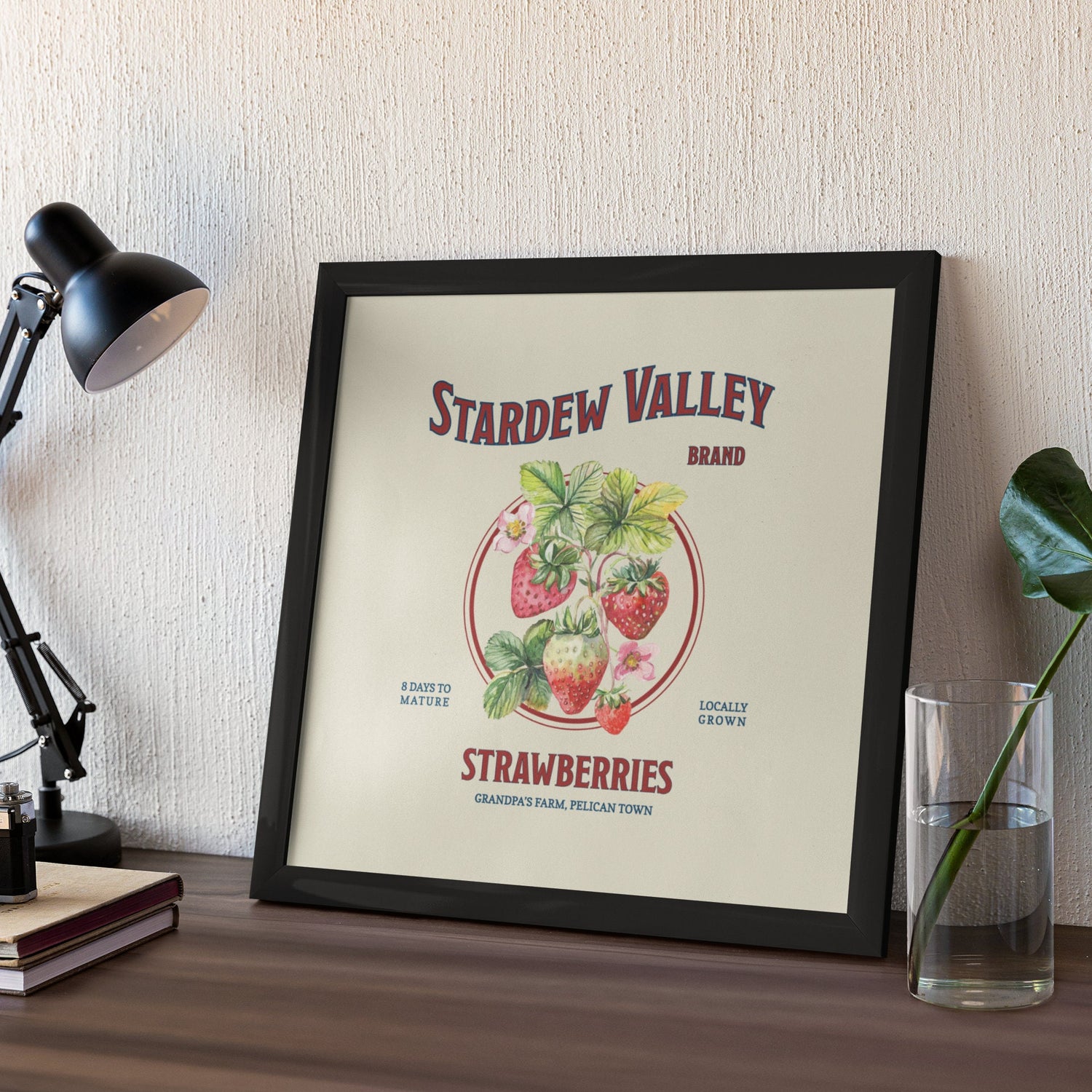 A small Stardew Valley Strawberries Print by New Save in a black frame on a desk.